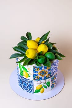 A round cake is decorated with lemons, green leaves, and ceramic tiles pattern. The cake is isolated on a beige background.