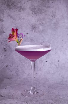 Elegant image of a pink cocktail in a glass with a flower garnish on a gray background, exuding class and sophistication.