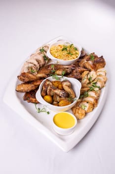 Assorted roasted meats, colorful vegetables, and golden potatoes garnished with fresh parsley and savory sauces on a white platter.