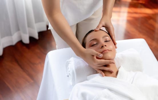 Caucasian woman enjoying relaxing anti-stress head massage and pampering facial beauty skin recreation leisure in dayspa modern light ambient at luxury resort or hotel spa salon. Quiescent