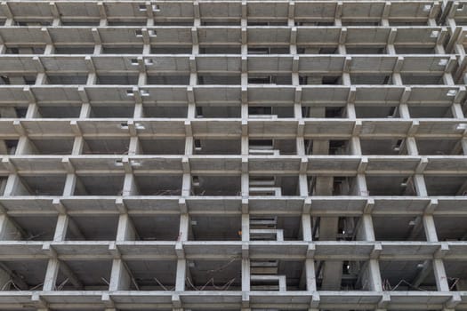 A large multi-storey apartment building is under construction, with a grey facade and a pattern of holes. Full-frame background. Low angle view,