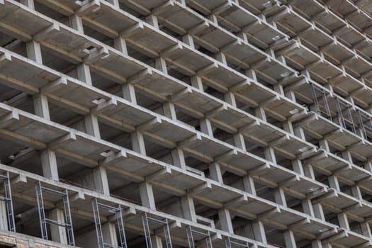 A large multi-storey apartment building is under construction, with a grey facade and a pattern of holes. Full-frame background. Low angle view,