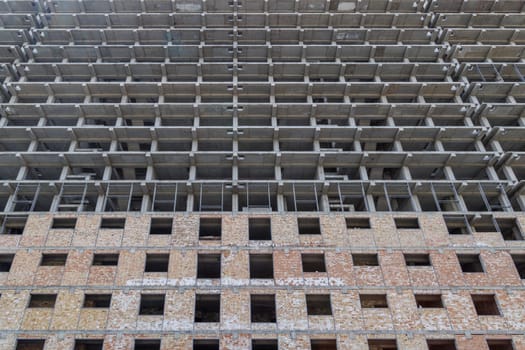 A large multi-storey apartment building is under construction, with a grey facade and a pattern of holes. Full-frame background. Low angle view,