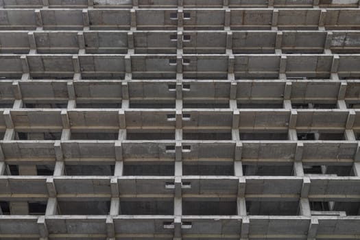 A large multi-storey apartment building is under construction, with a grey facade and a pattern of holes. Full-frame background. Low angle view,