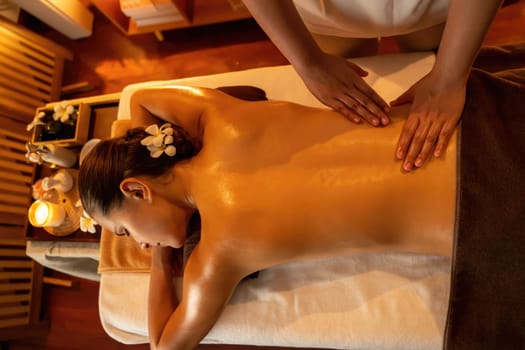 Caucasian woman customer enjoying relaxing anti-stress spa massage and pampering with beauty skin recreation leisure in warm candle lighting ambient salon spa at luxury resort or hotel. Quiescent