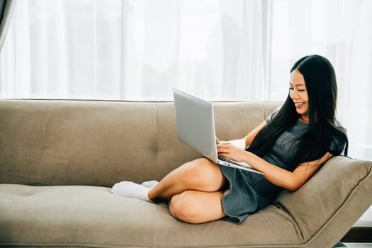 Relaxed woman on sofa uses laptop for ecommerce watching videos learning. Engaged in studying success and relaxation at home. Modern technology for education and shopping.