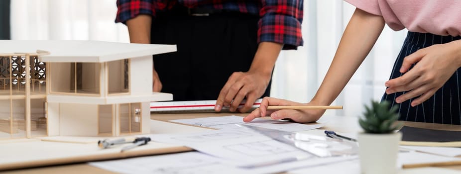 Smart architect engineer and interior designer working together and measuring house model by using ruler on meeting table with blueprint and architectural equipment. Teamwork concept. Burgeoning.