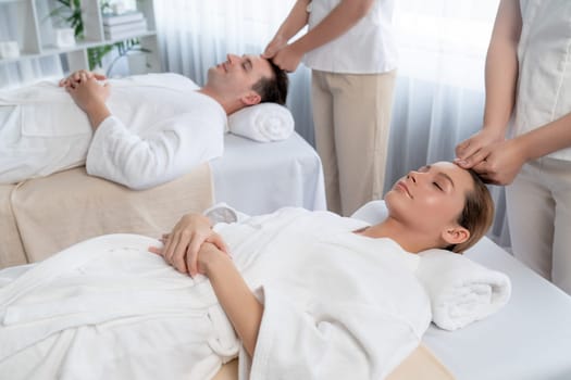 Caucasian couple enjoying relaxing anti-stress head massage and pampering facial beauty skin recreation leisure in dayspa modern light ambient at luxury resort or hotel spa salon. Quiescent