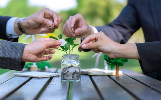 Business people put coin to money saving glass jar on outdoor table as sustainable money growth investment or eco-subsidize. Green corporate promot and invest in environmental awareness. Gyre