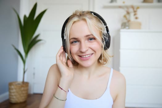 Portrait of good-looking young blond woman in wireless headphones, listens to podcast or favourite song, enjoys music in new earphones.