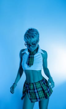 Sexy girl in an erotic school plaid skirt costume from a sex shop in blue neon light on copy paste background