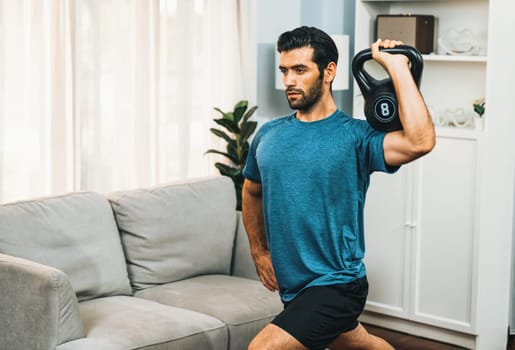 Athletic body and active sporty man lifting kettlebell weight for effective targeting muscle gain at gaiety home as concept of healthy fit body home workout lifestyle.