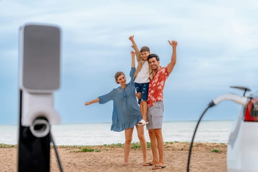 Family vacation trip traveling by the beach with eco-friendly electric car, lovely and cheerful family charging EV car battery on the seascape with green and sustainable energy. Perpetual