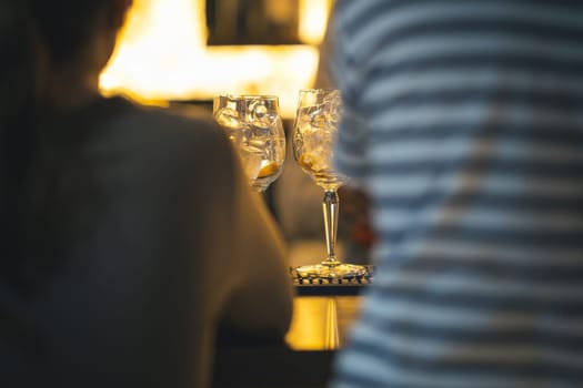 Two people are sitting at a bar with glasses of water in front of them. The glasses are half full and the people are looking at each other. Scene is relaxed and casual