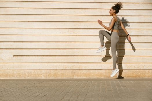 Female athlete in sportswear leaping in air with wall backdrop outdoors. Healthy lifestyle concept