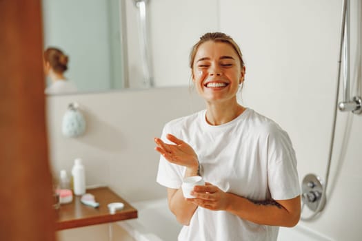 Smiling woman holding jar with skincare cream in hands. Home beauty routine