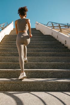 Back view of active female athlete in sportswear running on steps outdoors on a sunny day