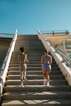 Two active female athlete friends in sportswear running on steps outdoors on a sunny day