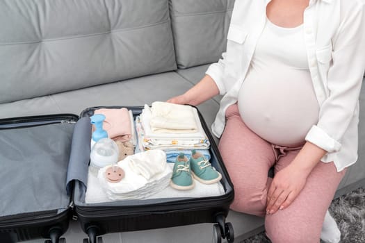 Folded things for the maternity hospital in a suitcase by a pregnant woman.