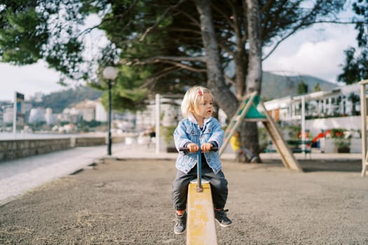 Little girl sits on a swing-balancer holding the handle. High quality photo