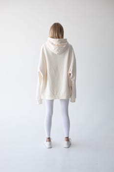 Blonde girl in a white hoodie and tights posing on a white background. High quality photo