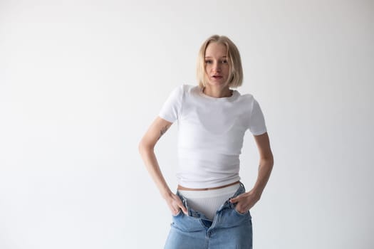 Beautiful blonde girl in a white T-shirt and blue jeans and sneakers posing on a white background. High quality photo