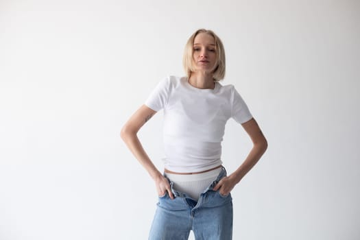 Beautiful blonde girl in a white T-shirt and blue jeans and sneakers posing on a white background. High quality photo