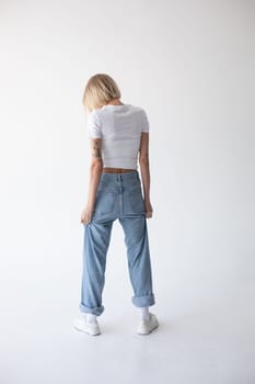 Beautiful blonde girl in a white T-shirt and blue jeans and sneakers posing on a white background. High quality photo