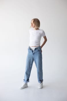 Beautiful blonde girl in a white T-shirt and blue jeans and sneakers posing on a white background. High quality photo