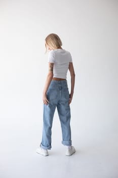 Beautiful blonde girl in a white T-shirt and blue jeans and sneakers posing on a white background. High quality photo