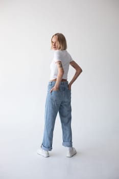 Beautiful blonde girl in a white T-shirt and blue jeans and sneakers posing on a white background. High quality photo