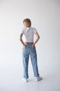 Beautiful blonde girl in a white T-shirt and blue jeans and sneakers posing on a white background. High quality photo