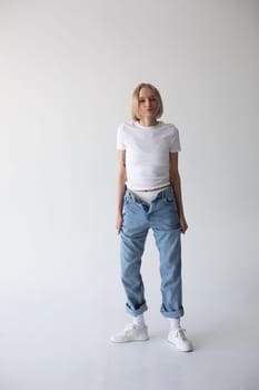 Beautiful blonde girl in a white T-shirt and blue jeans and sneakers posing on a white background. High quality photo