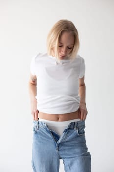 Beautiful blonde girl in a white T-shirt and blue jeans and sneakers posing on a white background. High quality photo