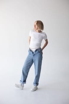 Beautiful blonde girl in a white T-shirt and blue jeans and sneakers posing on a white background. High quality photo