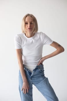 Beautiful blonde girl in a white T-shirt and blue jeans and sneakers posing on a white background. High quality photo