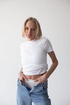 Beautiful blonde girl in a white T-shirt and blue jeans and sneakers posing on a white background. High quality photo