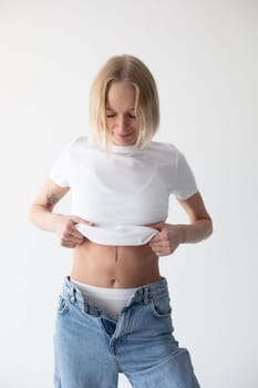 Beautiful blonde girl in a white T-shirt and blue jeans and sneakers posing on a white background. High quality photo