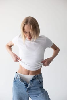 Beautiful blonde girl in a white T-shirt and blue jeans and sneakers posing on a white background. High quality photo