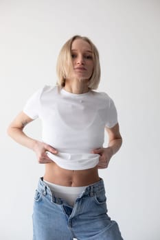 Beautiful blonde girl in a white T-shirt and blue jeans and sneakers posing on a white background. High quality photo