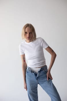 Beautiful blonde girl in a white T-shirt and blue jeans and sneakers posing on a white background. High quality photo