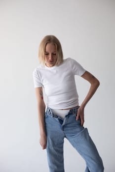 Beautiful blonde girl in a white T-shirt and blue jeans and sneakers posing on a white background. High quality photo