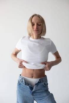 Beautiful blonde girl in a white T-shirt and blue jeans and sneakers posing on a white background. High quality photo