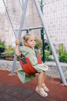 Little girl swings on a chain swing at the playground with her tongue hanging out. High quality photo