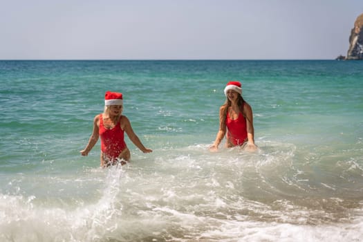 Women Santa hats ocean play. Seaside, beach daytime, enjoying beach fun. Two women in red swimsuits and Santa hats are enjoying themselves in the ocean waves