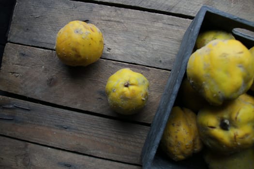 Fresh ripe organic quinces in a box on a vintage wooden table.