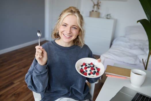 Portrait of young woman talking to audience, recording vlog on digital camera, showing her breakfast, talking about healthy food and lifestyle.