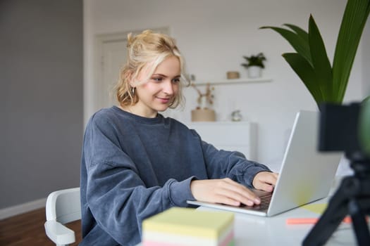 Portrait of young woman, student studying at home on remote education, working on laptop, typing on keyboard.