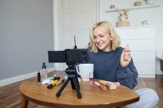 Portrait of blond smiling woman records a lifestyle blog, vlogger or makeup artist recording video for social media, holding mascara, reviewing beauty products for followers online.