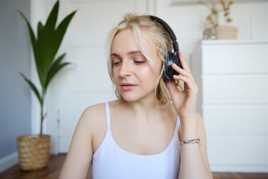 Portrait of good-looking young blond woman in wireless headphones, listens to podcast or favourite song, enjoys music in new earphones.